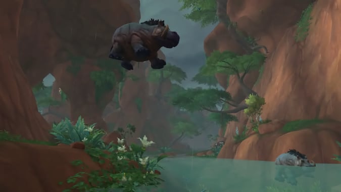 A wide shot of a hippo-like creature jumping into a river.