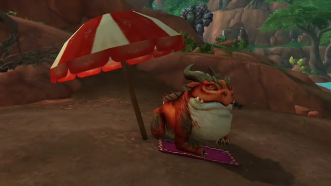 A horned red frog monster sits on a beach towel beneath a red and white umbrella.